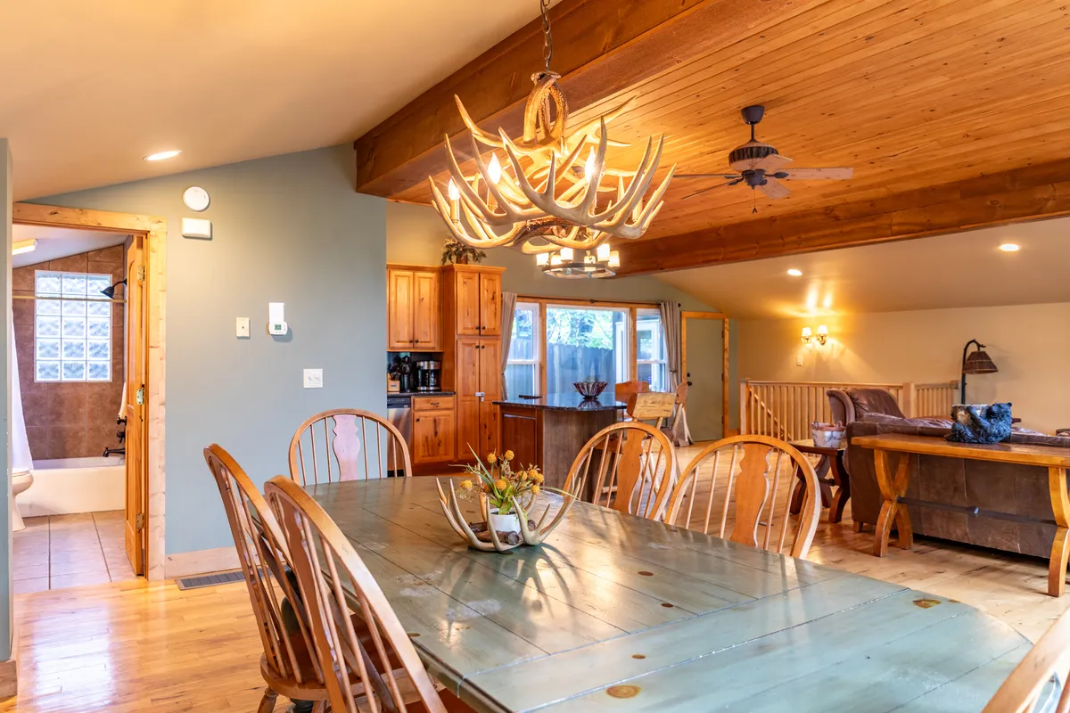 A spacious dining area with a large wooden table, an antler chandelier overhead, and comfortable chairs, all bathed in warm, ambient lighting. The setting suggests memorable gatherings and shared meals, reinforcing a sense of community and belonging.