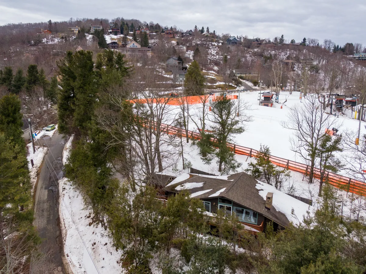 A wide view of the wooden lodge nestled in a snow-covered landscape, with orange fencing marking a ski area. The setting features the lodge set against a backdrop of white hills, inviting families to gather after outdoor adventures.