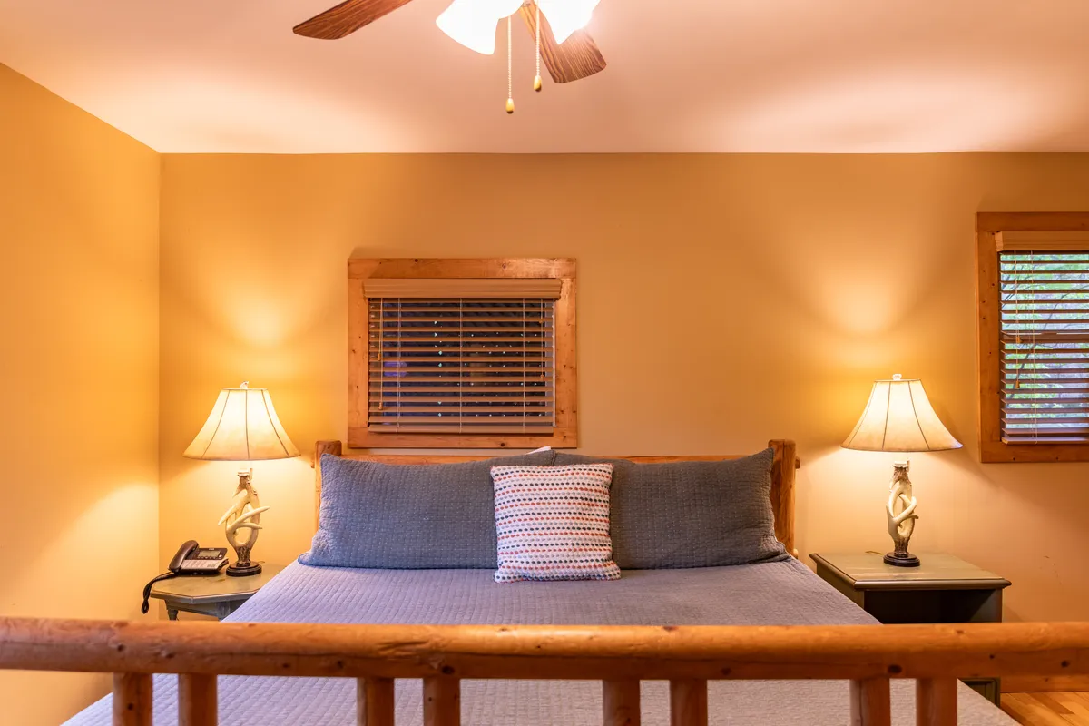 A serene bedroom featuring a comfortable bed with soft bedding, flanked by warm lamps on either side. Natural light gently pours in through a sizeable window, providing tranquil views and inviting a sense of calm.