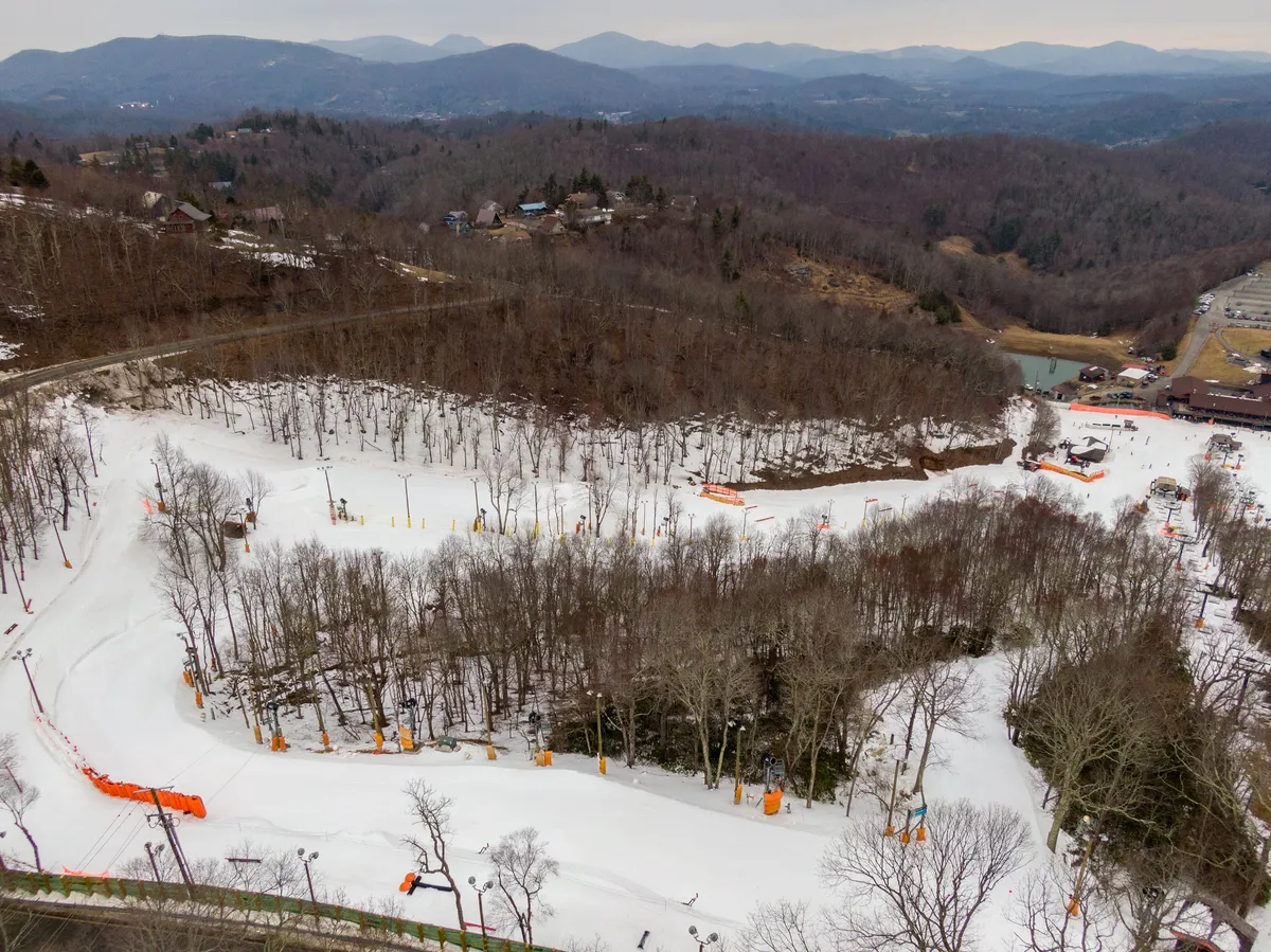 A dynamic view of the ski resort with snow-covered slopes, ski lifts ascending the mountain, and orange safety barriers lining the runs. The energy and excitement of winter sports are palpable, and the scenic mountain backdrop completes the picture of an active winter getaway.