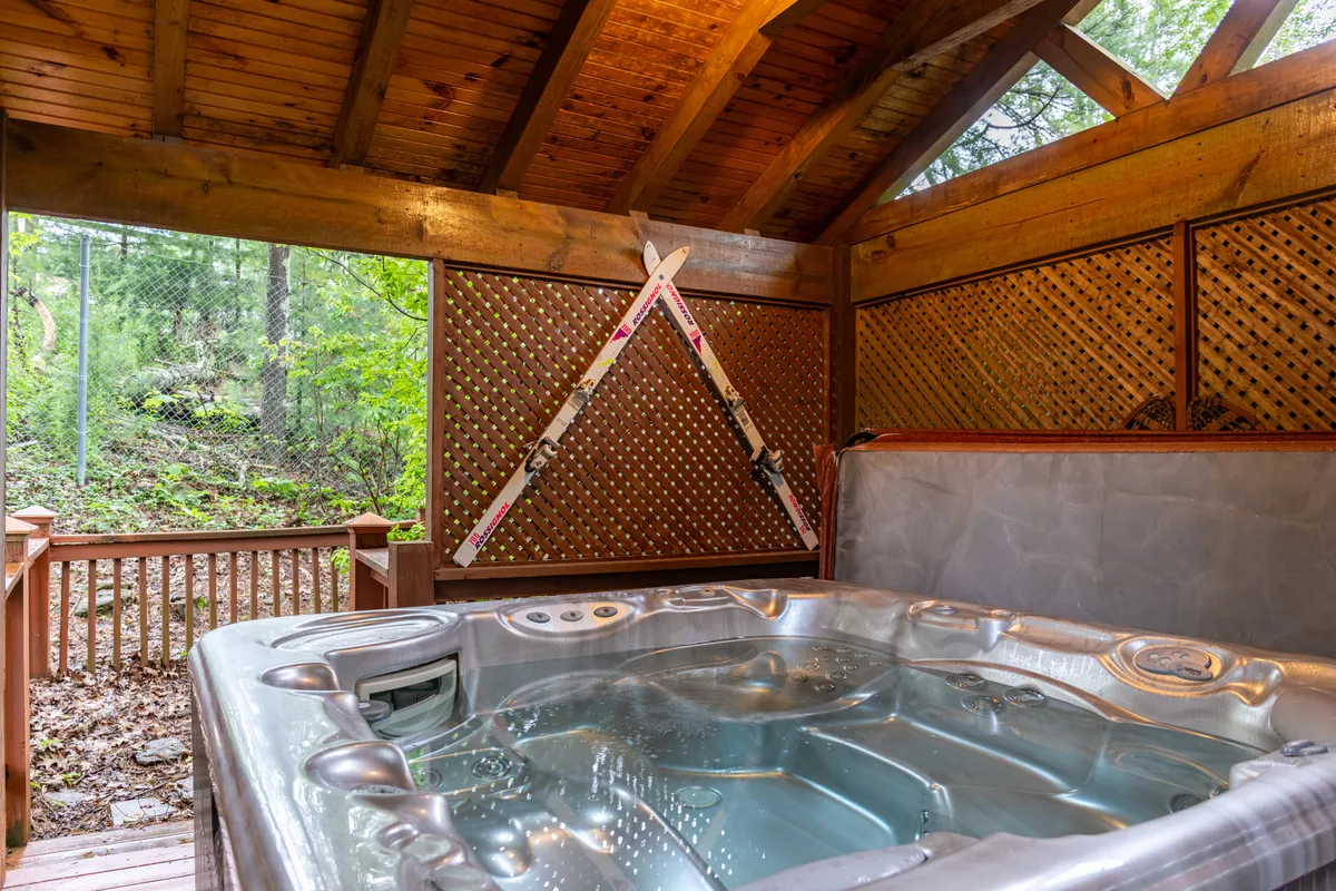 This interior image showcases a private hot tub set within a wooden structure, accented by decorative skis on the wall. Through the open sides, you see hints of natural surroundings, reinforcing the connection to the outdoors and mountain lifestyle. The hot tub is inviting, ideal for relaxing after a day of adventure, and the decor adds a cozy, alpine touch.