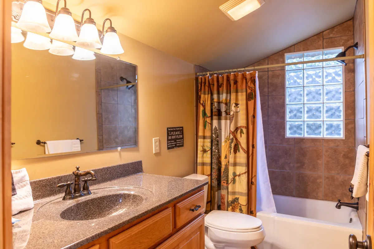 A full bathroom with a granite countertop, large mirror, decorative shower curtain, and a bathtub, all bathed in comfortable natural light. The space looks serene and functional for relaxing routines.