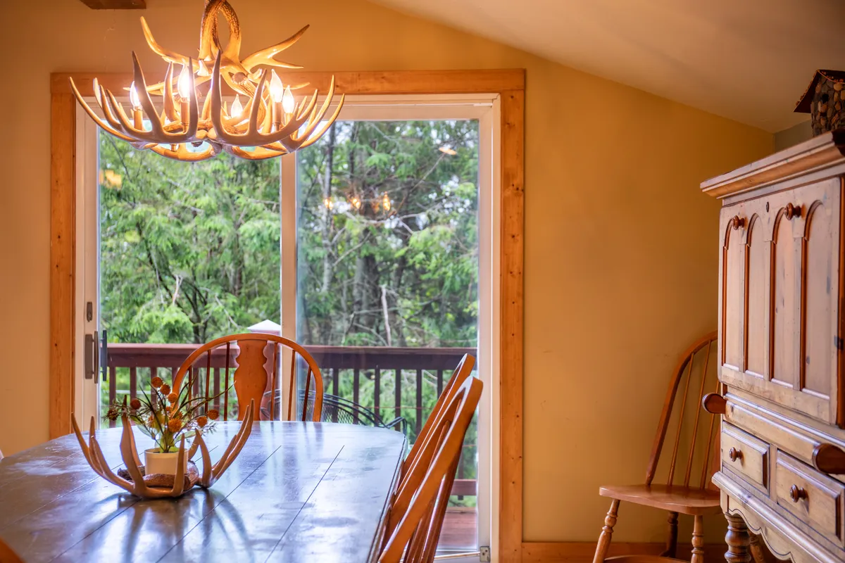 A cozy dining space with an antler chandelier, a welcoming table, and views through large glass doors that connect the interior to the outdoors. The natural light and inviting decor emphasize relaxation and connection with the surrounding mountain environment.