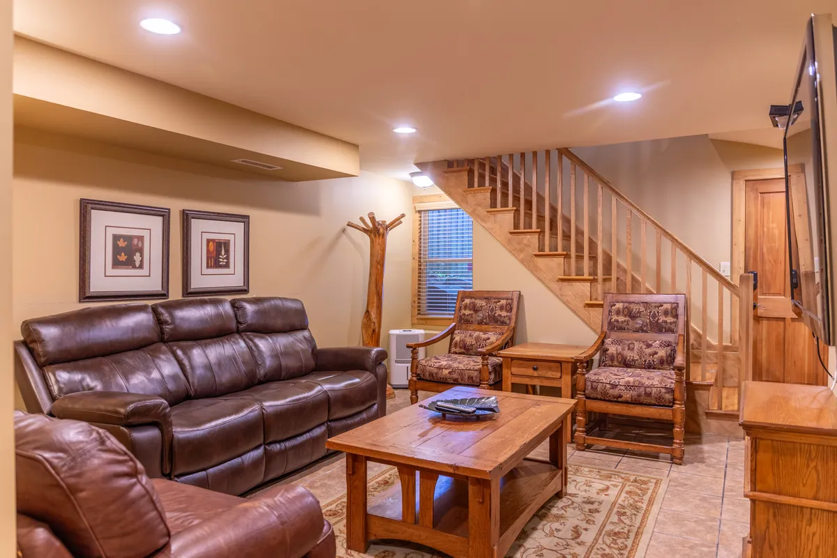 A welcoming interior scene with a leather sofa, wooden coffee table, staircase, and framed artwork on the wall. The setting evokes warmth and relaxation, with ample space for guests to unwind, socialize, and enjoy shared activities like movie nights or storytelling.