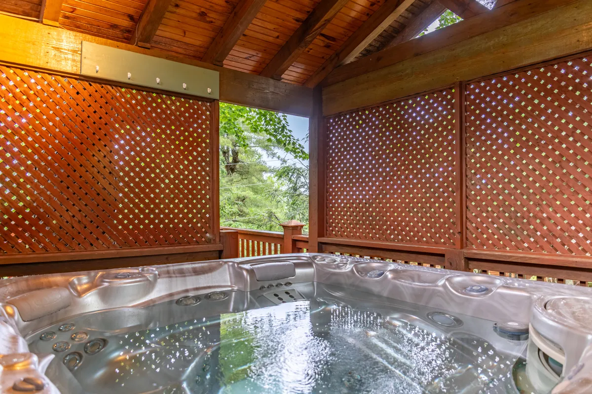 An inviting hot tub set on a wooden deck surrounded by lattice walls and natural greenery. This tranquil spot is perfect for relaxing after a day on the slopes, with the promise of warmth and comfort even in the heart of winter.