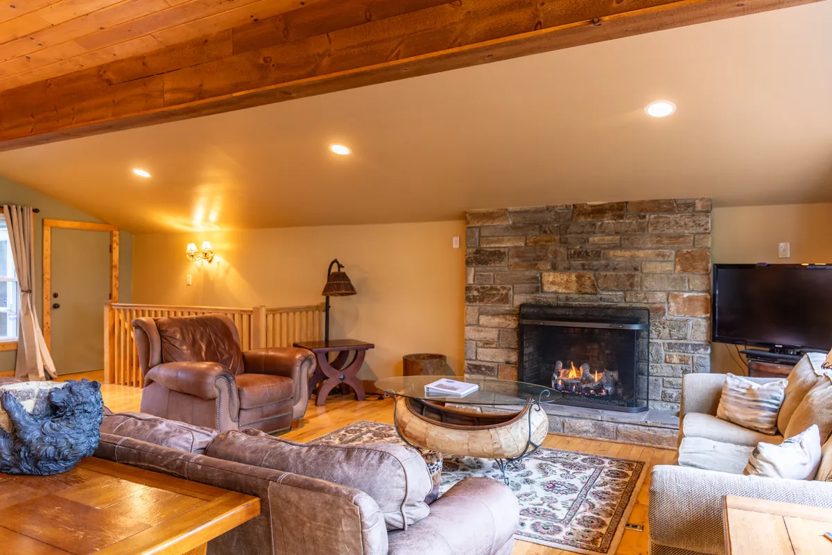This image captures a warm, inviting living space featuring a stone fireplace, plush seating area, and rustic wooden beams. The atmosphere is cozy and welcoming, suggesting a place where guests can relax and socialize comfortably.